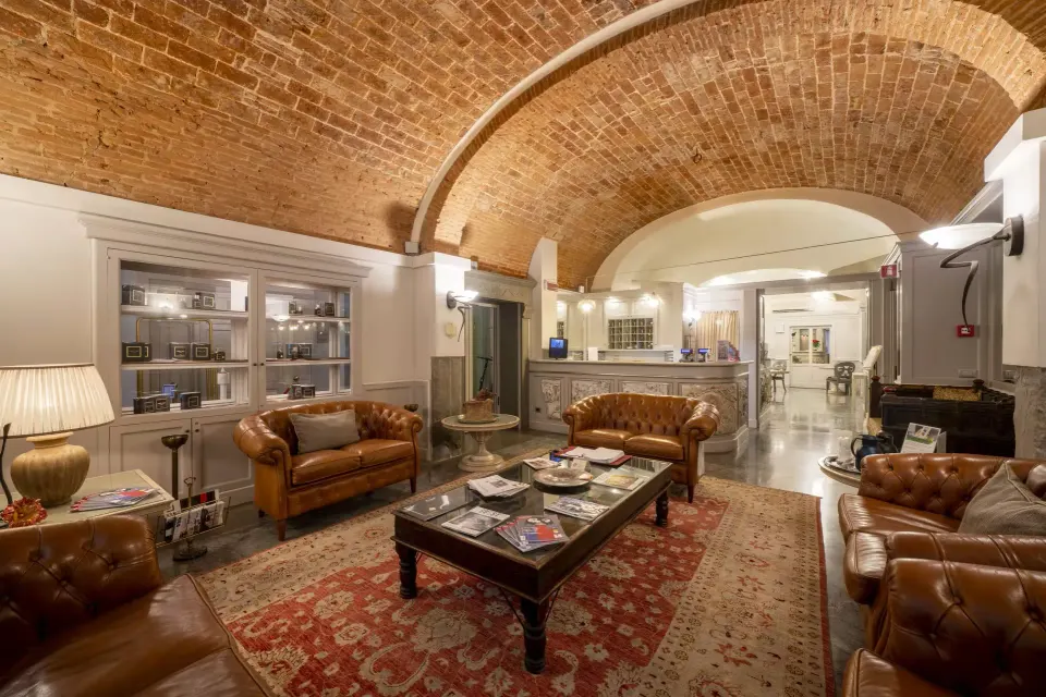 A hotel lounge under a vaulted brick ceiling, with leather armchairs, a low table and a patterned rug.